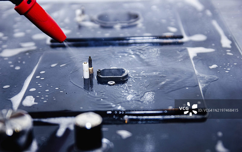 红色喷嘴特写，向泡沫覆盖的炉灶表面喷洒水。图片素材