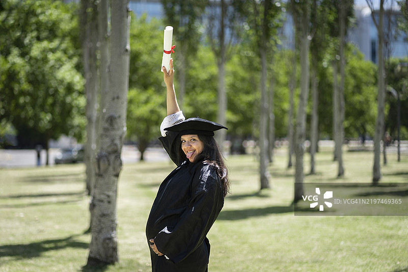 穿着长袍和学位帽的拉丁裔孕妇展示她的学位证书图片素材