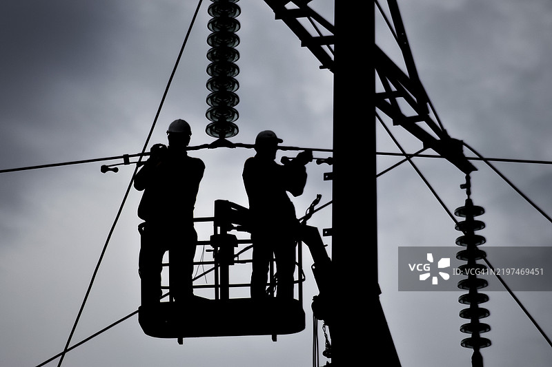 电工在天空的映衬下修理电力线。哈萨克斯坦，阿特劳，亚洲图片素材