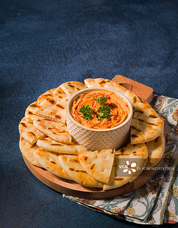 高角度视图的红椒鹰嘴豆泥，周围是切片的烤皮塔饼，背景为深蓝色表面，地点：美国弗吉尼亚州马纳萨斯图片素材