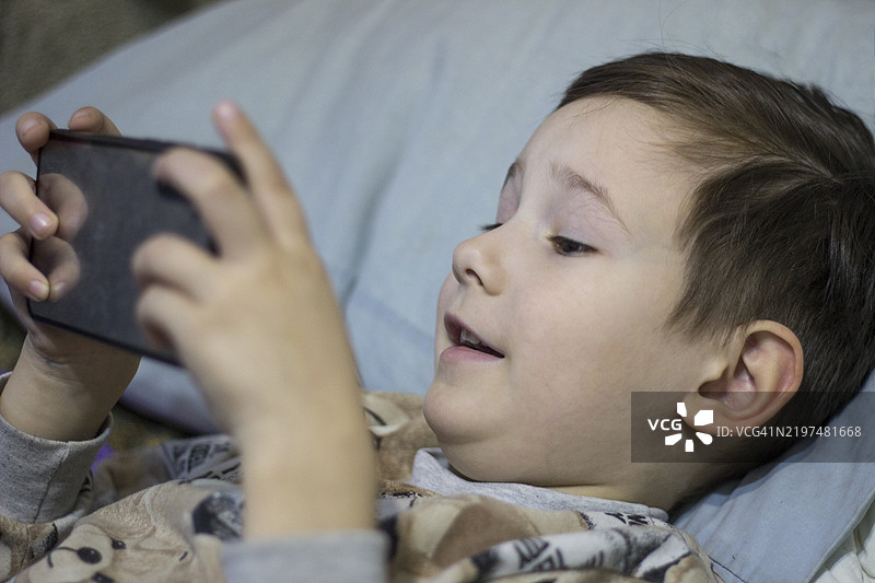 一个孩子躺在床上玩手机游戏图片素材