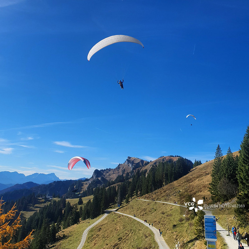 人们在晴朗的蓝天上滑翔伞飞越山脉图片素材