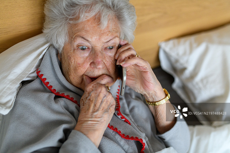 惊恐的老年女性正在拨打电话。针对老年人的电话诈骗。图片素材