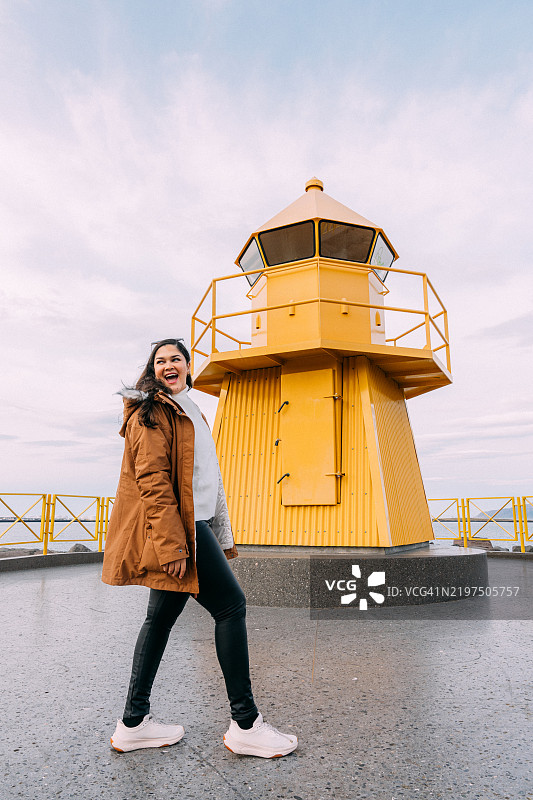 在冰岛雷克雅未克的黄色霍夫迪港灯塔前，快乐的多米尼加旅游影响者。图片素材