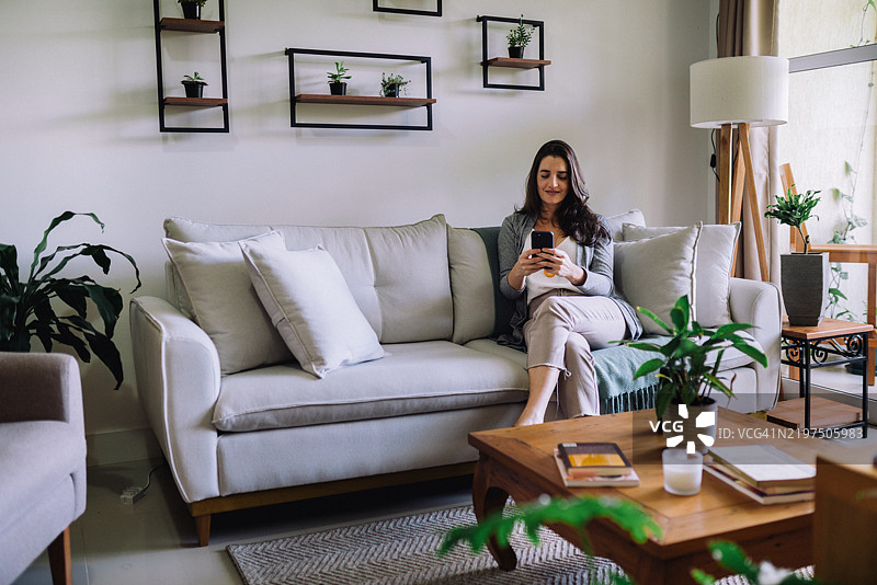 正面视角的女性坐在客厅沙发上进行视频通话图片素材