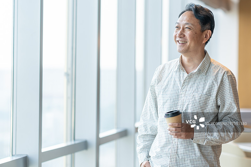 亚洲中年男性高管站在办公室窗前图片素材