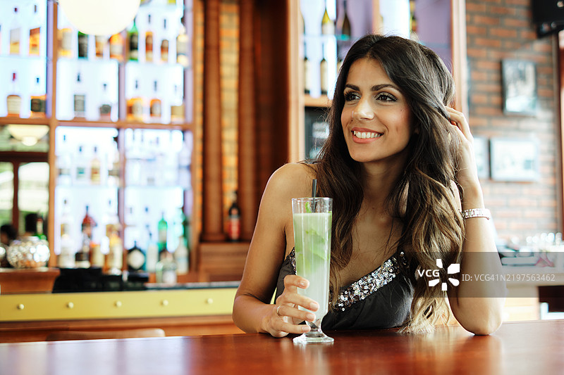 一位美丽的年轻女性坐在咖啡馆里喝着她的莫吉托。图片素材