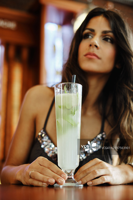 一位美丽的年轻女性坐在咖啡馆里喝着她的莫吉托。图片素材