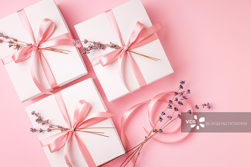 三个白色礼品盒用粉色丝带绑扎，搭配薰衣草装饰，背景为粉色。图片素材