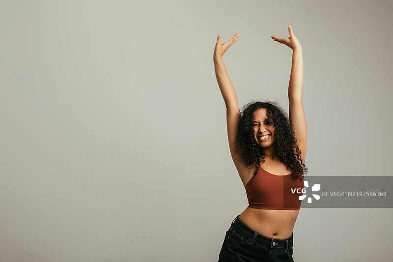 快乐的女性穿着时尚休闲服，举起双臂庆祝图片素材