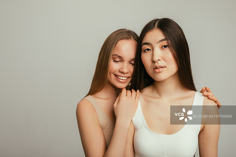 两位自然美丽的欧洲和亚洲女性在摄影棚中一起摆姿势的肖像图片素材