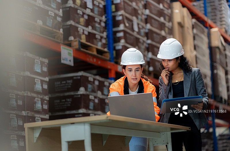 仓库运营中的团队合作——仓库经理与同事讨论计算机上的先进先出库存安排。高效的供应链规划、货运运输、制造物流和工业分销设施中的质量控制。图片素材