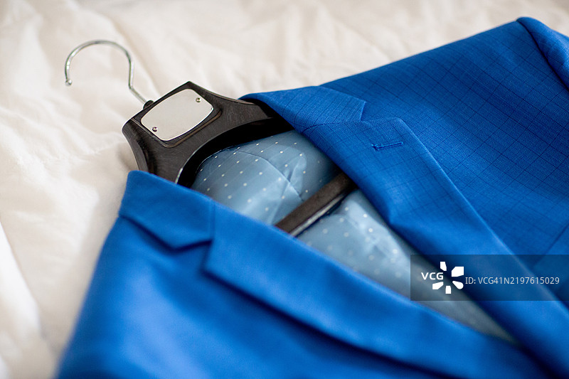 蓝色夹克挂在黑色衣架上，放在床上图片素材