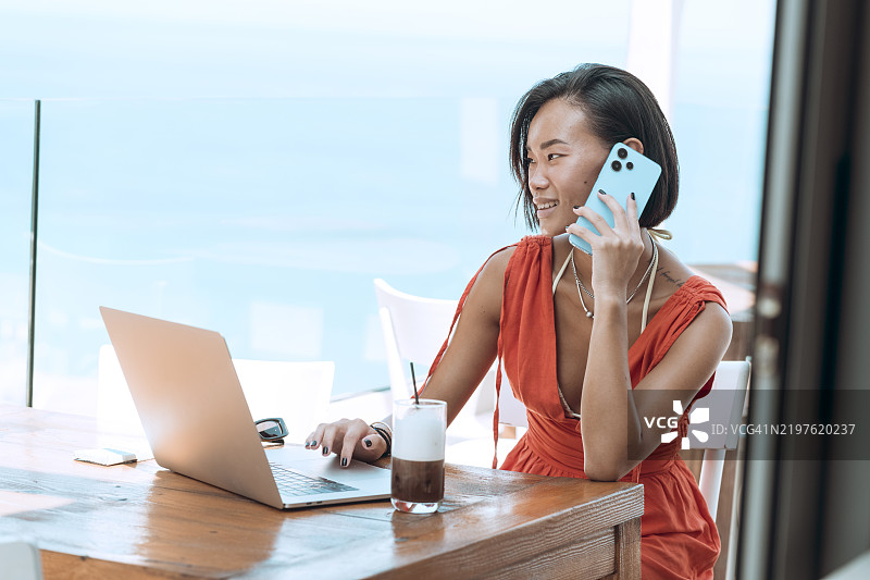 年轻女性在海边咖啡馆使用笔记本电脑图片素材