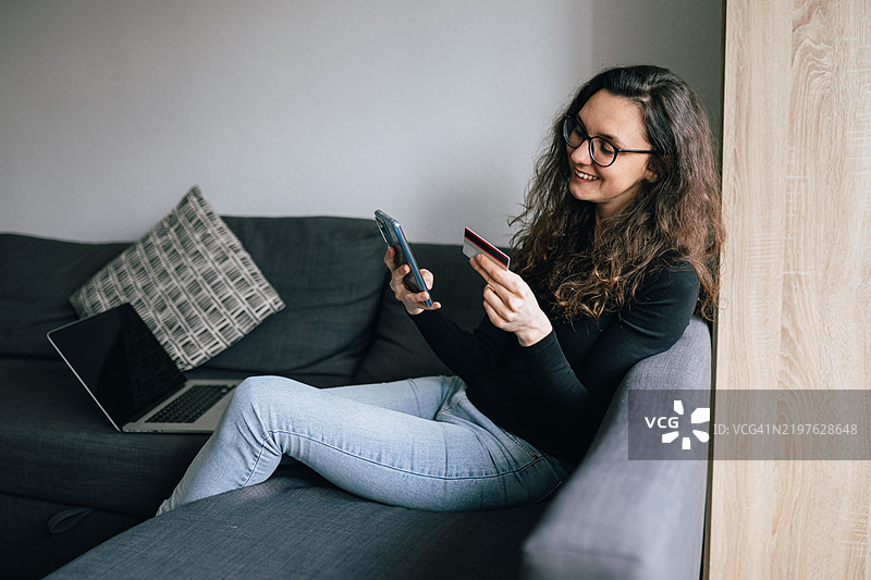 微笑的女性在家中使用智能手机和信用卡进行在线购物图片素材
