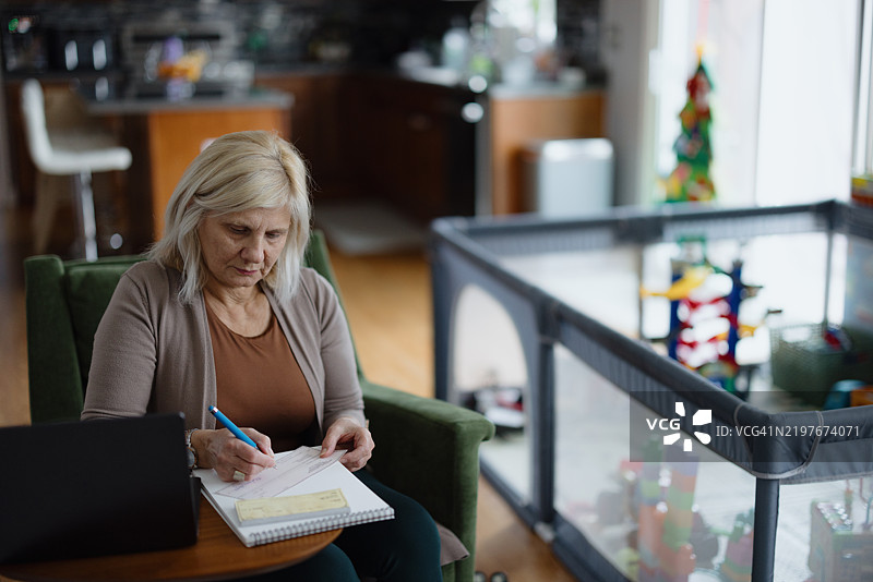 女性在家中使用支票簿和笔记本电脑管理财务图片素材