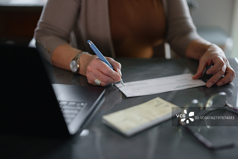 女性在办公桌上靠近笔记本电脑签署个人支票图片素材