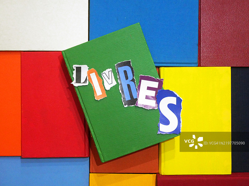 用撕碎的纸张拼成的不同字母写成的法语单词“LIVRES”(书籍),放置在多彩的书籍上。图片素材