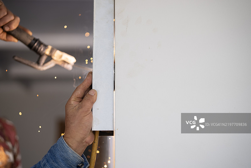 一名工人在室内焊接金属框架，产生明亮的火花。该图像捕捉了在建筑或修理环境中精确焊接的场景。图片素材