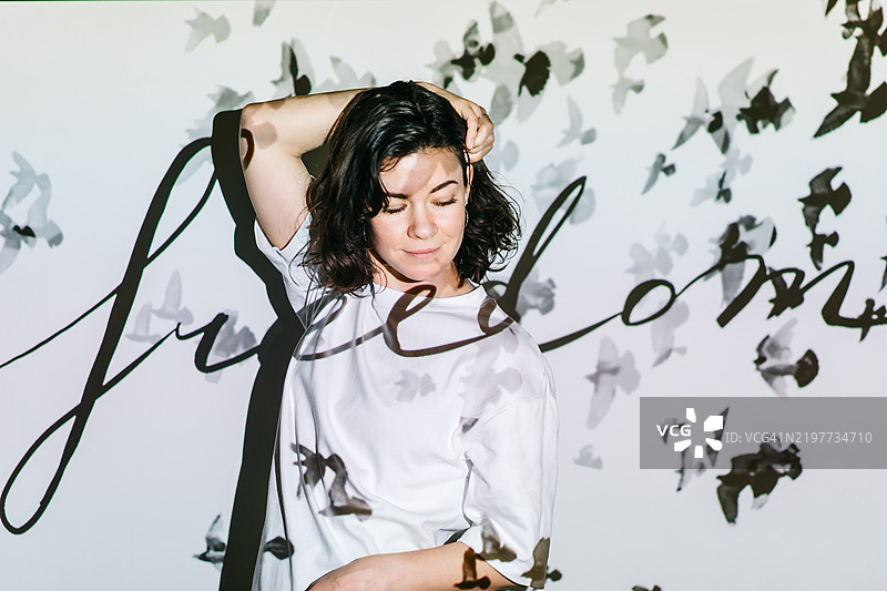 一位女性梦想家站在白色墙壁前，墙上投影着飞翔的鸟和“自由”这个词。图片素材