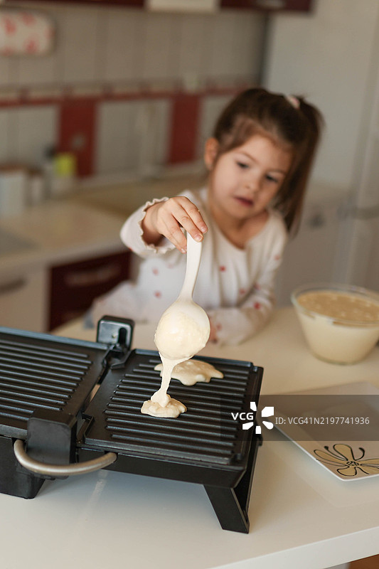 一个女孩将煎饼混合物倒在加热的煎锅上。图片素材