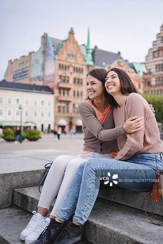 两位微笑的女性坐在瑞典马尔默的台阶上拥抱在一起图片素材