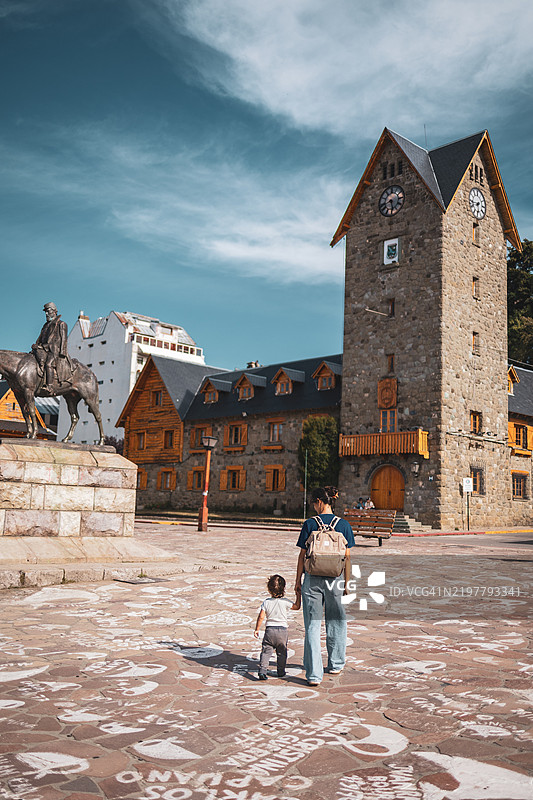 在巴塔哥尼亚的圣卡洛斯·德·巴里洛切，阳光明媚的天空下，家庭在历史建筑环绕的风景广场上探索。图片素材