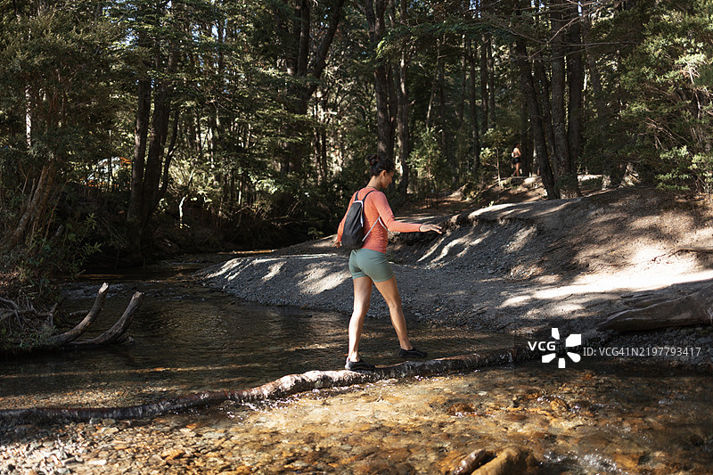 女人在森林小径上走过一根木头横跨的小溪图片素材