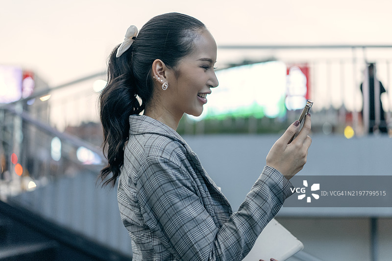 美丽的东南亚年轻女性在城市环境中使用智能手机，傍晚时分。图片素材