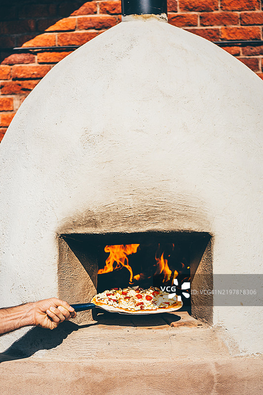 一个男人在木火烤炉中烘焙比萨。图片素材