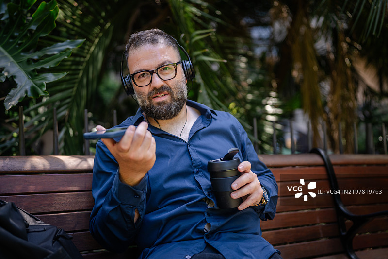 男子在悉尼郁郁葱葱的公园长椅上享受咖啡和交谈，放松身心。图片素材