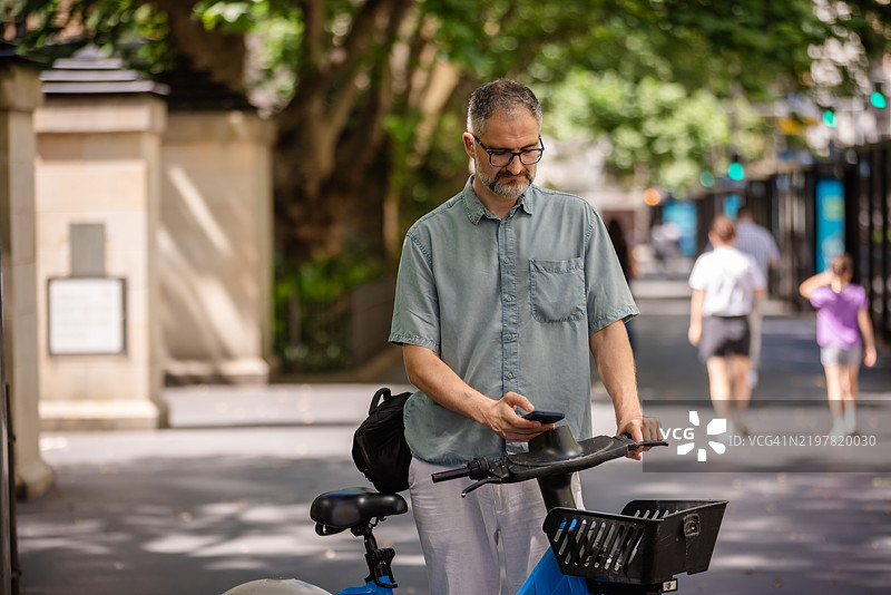 男子在繁忙的悉尼街道上停放自行车时使用手机，正值下午。图片素材