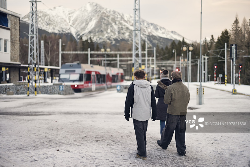 母亲和三个青少年在雪山车站Štrbské Pleso走向火车。图片素材