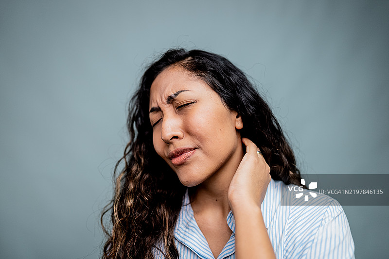 年轻女性在灰色背景下感到颈部疼痛图片素材