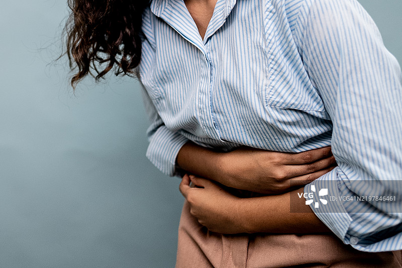 一位女性在灰色背景下腹部疼痛的特写镜头图片素材