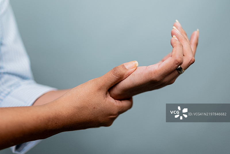 一位女性在灰色背景下按摩她的手腕特写镜头图片素材