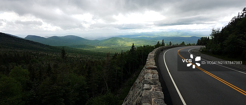 空旷的道路穿过树木，背后是黑暗的天空和山脉，纽约州威尔明顿，美国图片素材
