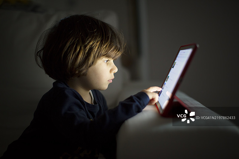 孩子在昏暗的房间里使用平板电脑，正值傍晚时分图片素材