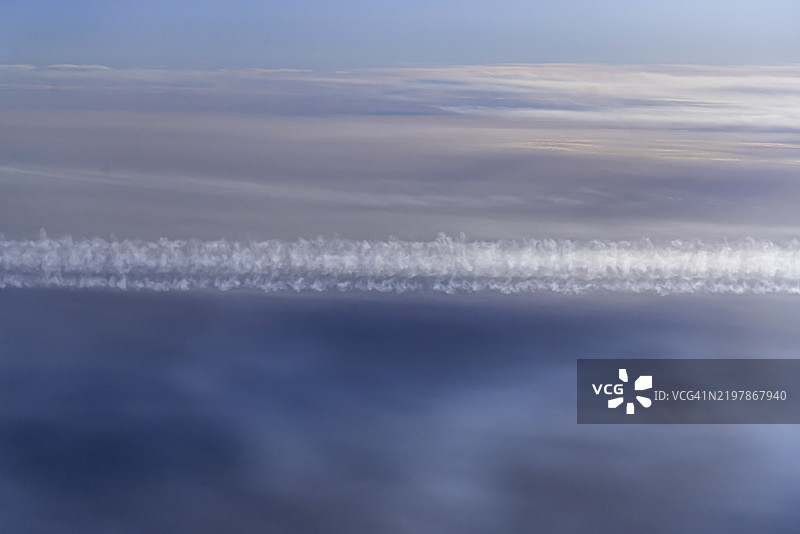 从飞机窗户俯瞰波斯湾。阳光和云彩映照在海面上。飞机飞翔在云层之上,留下了水汽轨迹。搭乘阿提哈德航空的航班。阿布扎比,阿拉伯联合酋长国,亚洲。图片素材