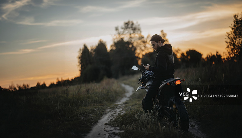 黄昏时分，一名骑摩托车的男子在乡间小路上，四周被大自然环绕。图片素材