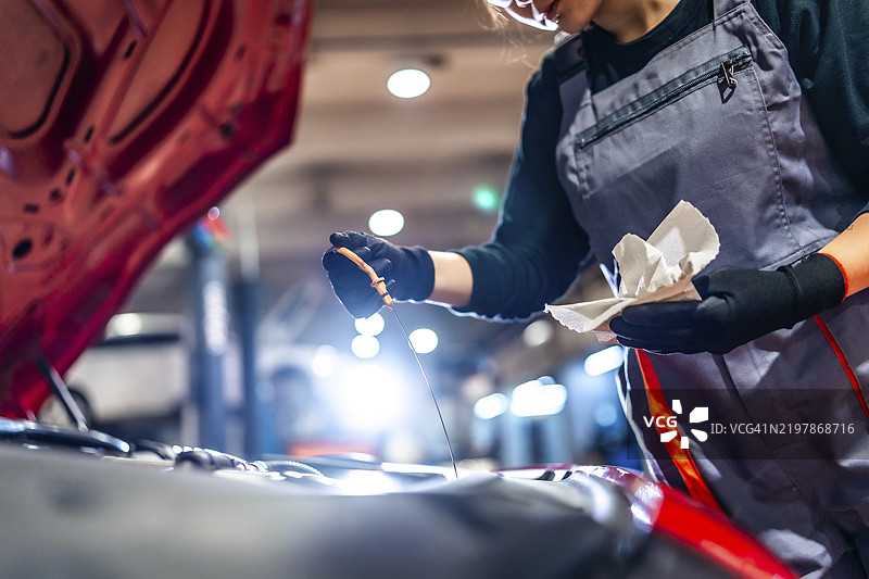 专业女性机械师在汽车修理店检查发动机油位，使用油尺和抹布。图片素材