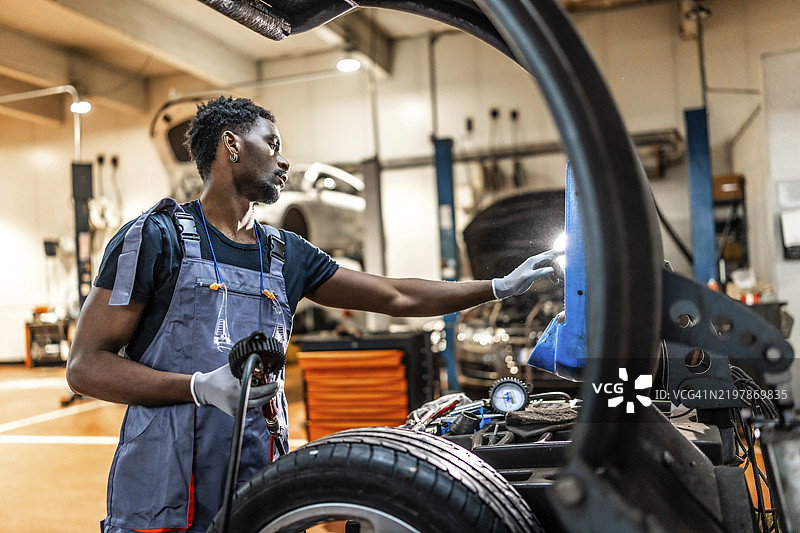 年轻的机械师在专业汽车修理店进行汽车维护，检查轮胎和底盘。图片素材
