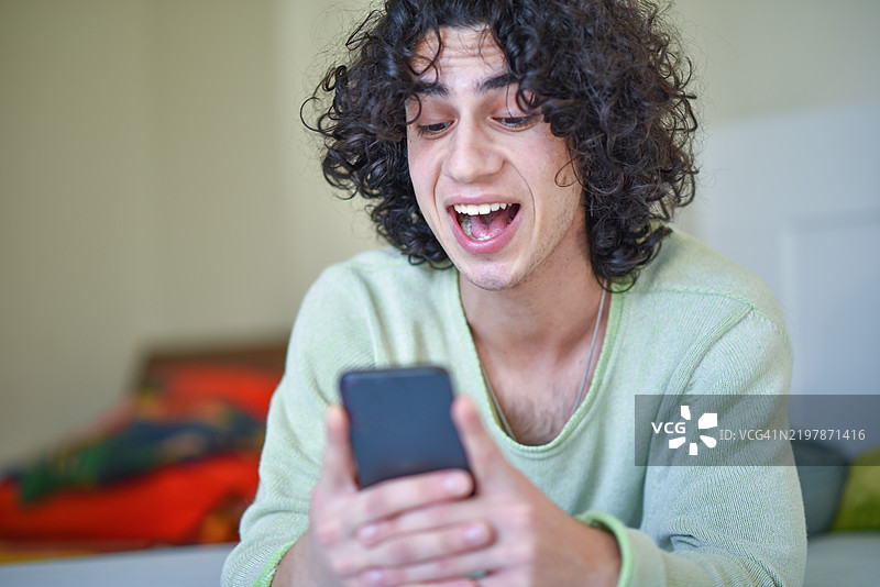 年轻男子在室内兴奋地使用智能手机。图片素材