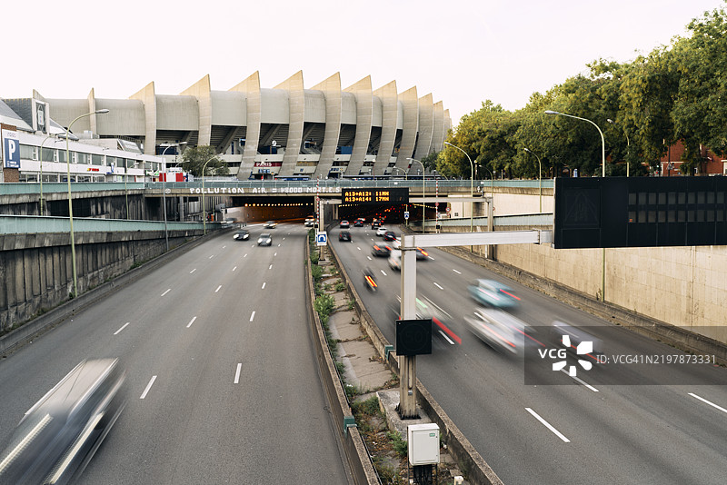 巴黎市体育场外观的正面视图，阳光明媚的日子里道路上有汽车。图片素材