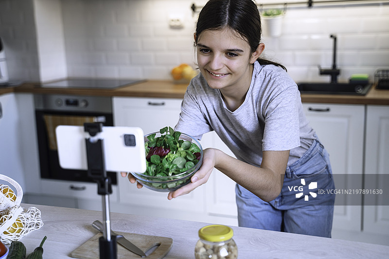 年轻女孩在智能手机上展示新鲜沙拉图片素材