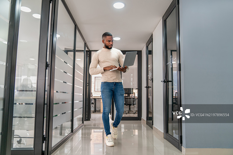 商人在办公室走动，手里拿着一台笔记本电脑图片素材