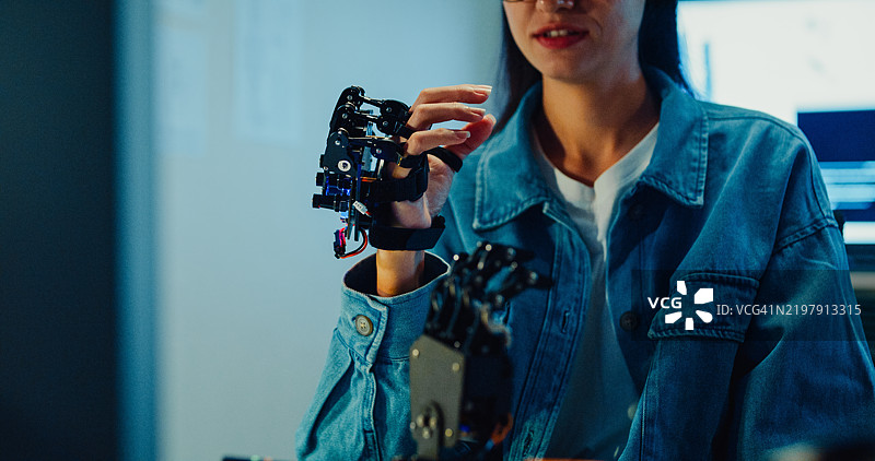 年轻女性工程师在夜间的科技实验室里加班，手势指向机械臂。机器学习、计算机制造、创新与创造力。人工智能与机器人开发。图片素材