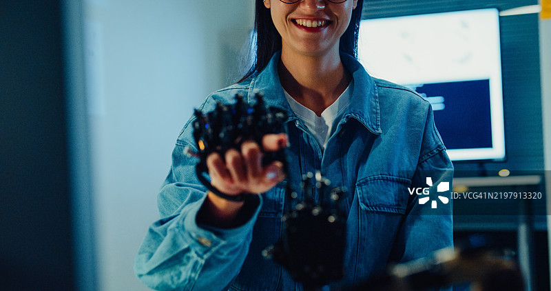 年轻女性工程师在夜间的科技实验室里加班，手势指向机械臂。机器学习、计算机制造、创新与创造力。人工智能与机器人开发。图片素材