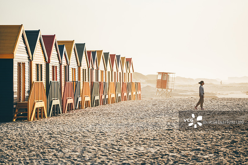 一位女性在穆伊森堡的冲浪角附近走过五彩缤纷的海滩小屋。图片素材