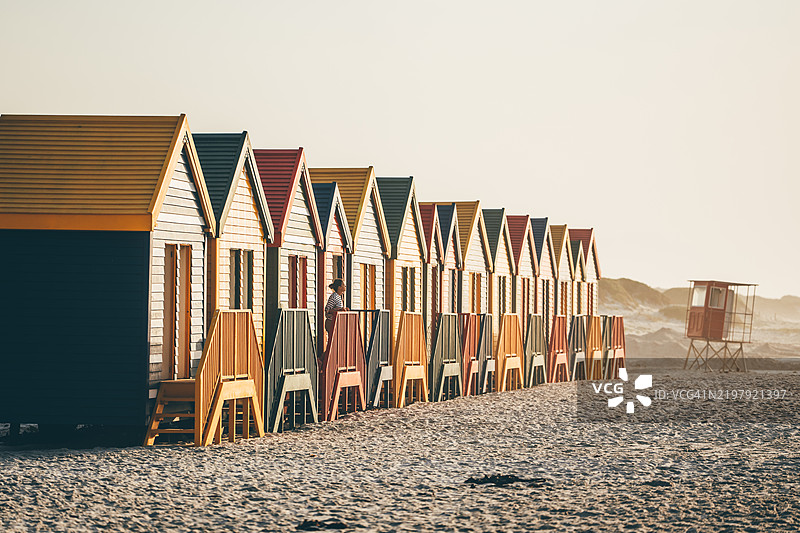 一位女性在穆伊森堡的冲浪角附近走过五彩缤纷的海滩小屋。图片素材